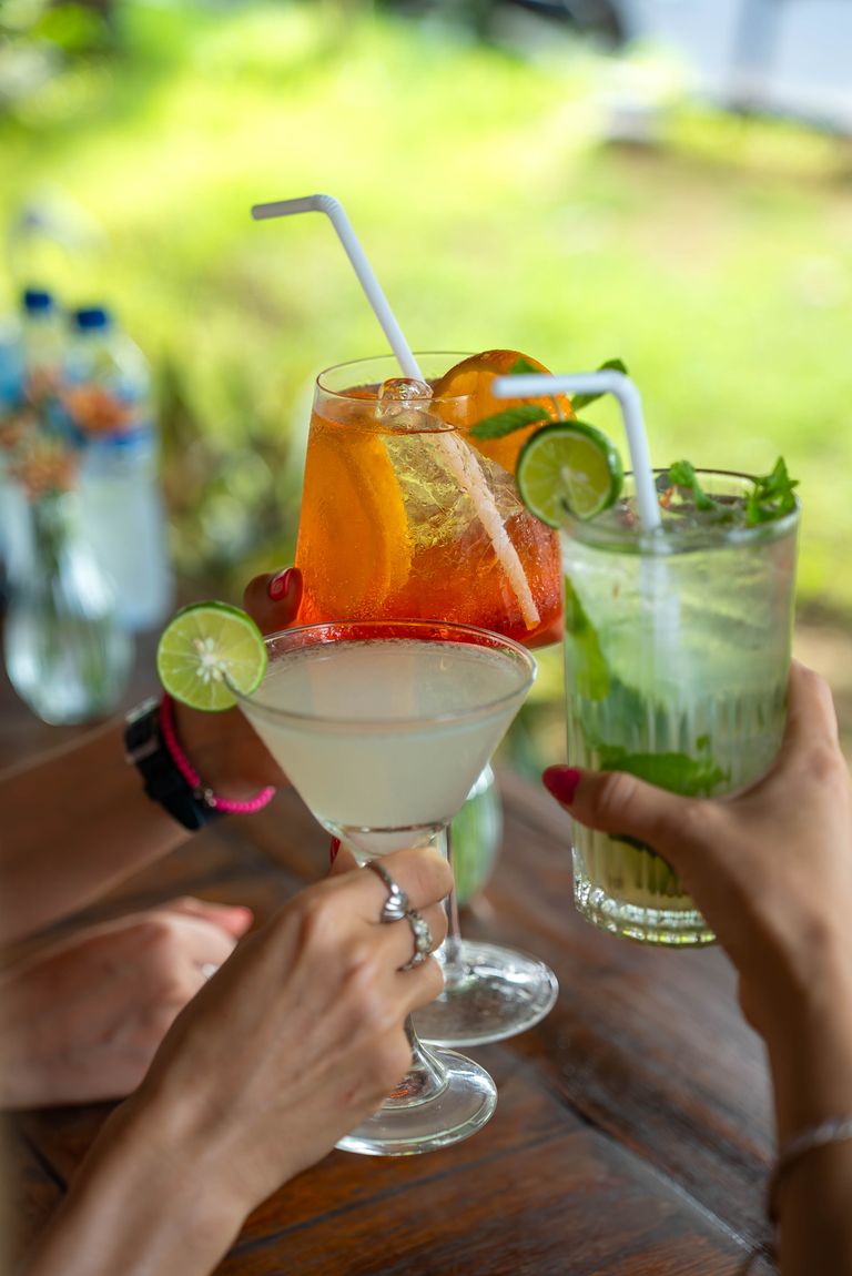 Three hands toasting with vibrant cocktails in an outdoor setting, perfect for summer gatherings.