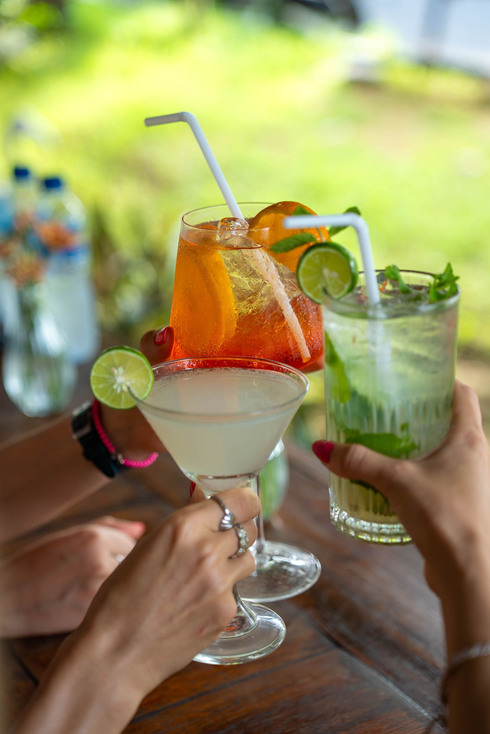 Three hands toasting with vibrant cocktails in an outdoor setting, perfect for summer gatherings.